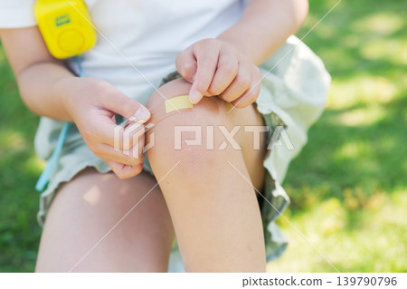 Elementary school student putting a bandage on his knee Elementary school student putting a bandage on his knee 139790796