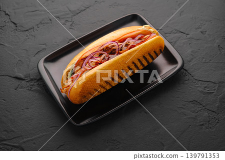 Grilled hot dog with onions and toppings on a black plate 139791353