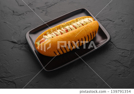 Hot dog served on a black plate with toppings at a restaurant 139791354