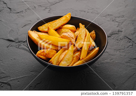 Crispy potato wedges served in a black bowl on a dark surface Crispy potato wedges served in a black bowl on a dark surface 139791357
