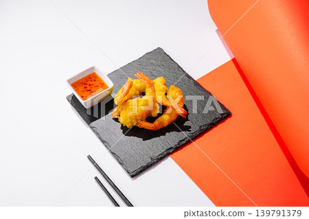 Crispy shrimp served on a black plate with sauce on a colorful table Crispy shrimp served on a black plate with sauce on a colorful table 139791379