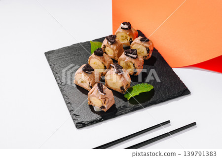 Dessert sushi rolls made with chocolate and banana with unique ingredients and presented on black slate Dessert sushi rolls made with chocolate and banana with unique ingredients and presented on black slate 139791383