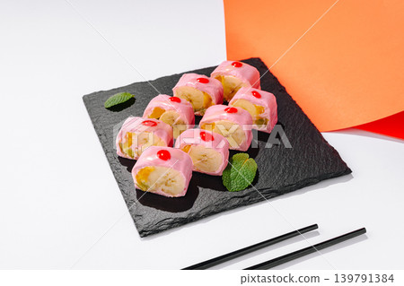 Sushi rolls with chocolate and banana arranged on a black plate with red toppings and chopsticks Sushi rolls with chocolate and banana arranged on a black plate with red toppings and chopsticks 139791384