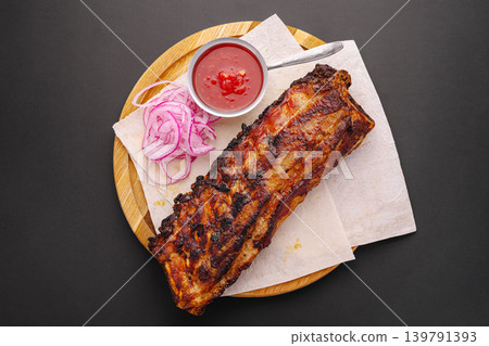 Grilled pork ribs with sliced onions and sauce on a wooden board Grilled pork ribs with sliced onions and sauce on a wooden board 139791393