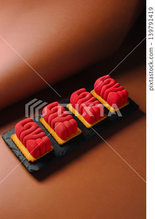 Red sweets arranged on a black plate on a brown surface in a dessert setting Red sweets arranged on a black plate on a brown surface in a dessert setting 139791419