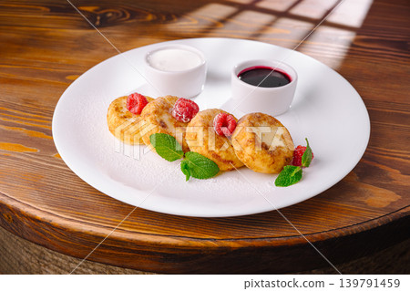 Freshly prepared cheese pancakes served with cream and berry sauce Freshly prepared cheese pancakes served with cream and berry sauce 139791459