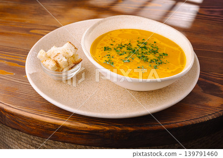 Soup served with bread on a round plate at a wooden table in daylight Soup served with bread on a round plate at a wooden table in daylight 139791460