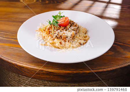 Pasta dish with sauce and cheese served on a white plate on wooden table Pasta dish with sauce and cheese served on a white plate on wooden table 139791468