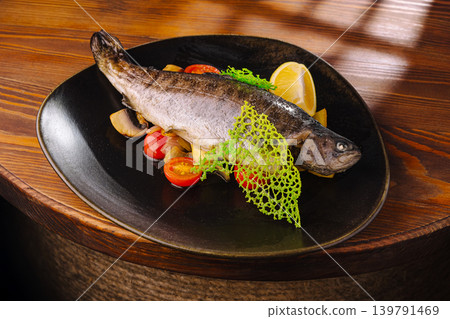 Grilled fish served on a black plate with vegetables and lemon Grilled fish served on a black plate with vegetables and lemon 139791469