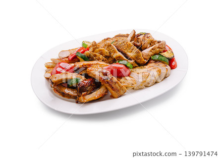 Grilled chicken, pork ribs, and vegetables served on a white plate at a dinner table 139791474