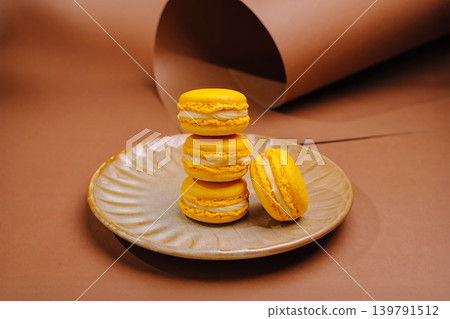 Yellow macarons stacked on a plate in a simple setup on a brown backdrop Yellow macarons stacked on a plate in a simple setup on a brown backdrop 139791512