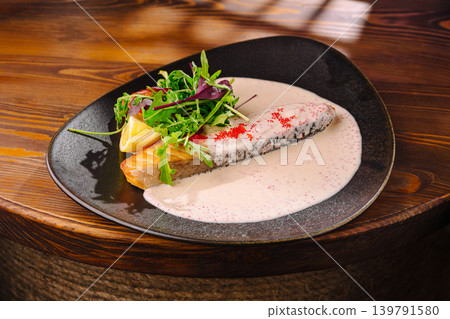 Dish of salmon with sauce and salad on a plate in a restaurant setting Dish of salmon with sauce and salad on a plate in a restaurant setting 139791580