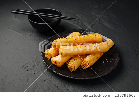 Delicious spring rolls on a black plate with chopsticks and a bowl Delicious spring rolls on a black plate with chopsticks and a bowl 139791603