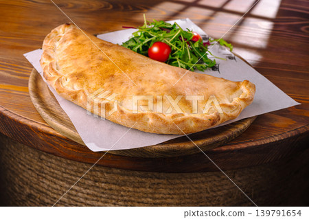 Freshly baked calzone with salad on a wooden table in a restaurant setting Freshly baked calzone with salad on a wooden table in a restaurant setting 139791654