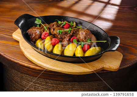 Warm dish with meat and potatoes served on a wooden table Warm dish with meat and potatoes served on a wooden table 139791658