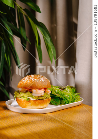 Fresh shrimp burger with salad on a wooden table next to a plant Fresh shrimp burger with salad on a wooden table next to a plant 139791683