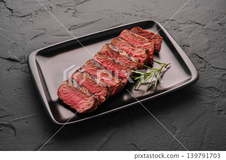Grilled veal steak served on black plate with fresh rosemary garnish in kitchen Grilled veal steak served on black plate with fresh rosemary garnish in kitchen 139791703