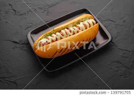 Fresh hot dog served on black plate with toppings and condiments Fresh hot dog served on black plate with toppings and condiments 139791705