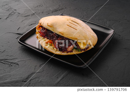 Delicious flatbread filled with various ingredients on a black plate Delicious flatbread filled with various ingredients on a black plate 139791706