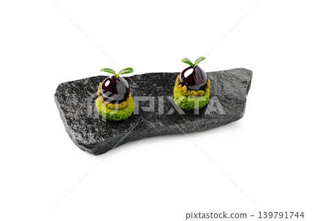 Delicate food creation on a black stone plate with green and dark elements Delicate food creation on a black stone plate with green and dark elements 139791744