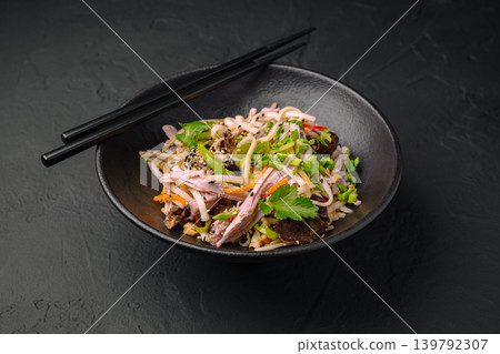 Noodle dish with vegetables and meat in a black bowl with chopsticks Noodle dish with vegetables and meat in a black bowl with chopsticks 139792307