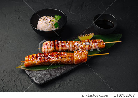 Grilled salmon skewers served with rice and dipping sauce in a dark setting Grilled salmon skewers served with rice and dipping sauce in a dark setting 139792308