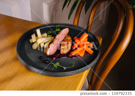 Duck dish served with vegetables on a black plate in a cozy setting Duck dish served with vegetables on a black plate in a cozy setting 139792335