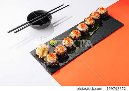 Sushi rolls on a black plate with chopsticks and soy sauce bowl on the side Sushi rolls on a black plate with chopsticks and soy sauce bowl on the side 139792352