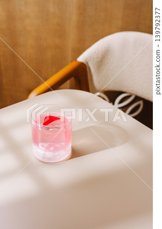 Pink cocktail with rose petal and ice cube on a table with a chair in a warm indoor space during daylight Pink cocktail with rose petal and ice cube on a table with a chair in a warm indoor space during daylight 139792377