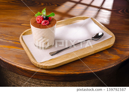 Tiramisu dessert with raspberries in glass on tray at a dining table in a cafe Tiramisu dessert with raspberries in glass on tray at a dining table in a cafe 139792387
