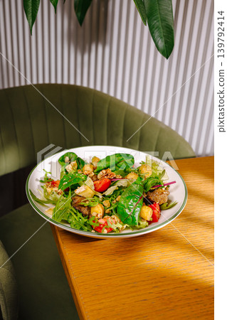 Fresh salad on a wooden table in a cozy dining area with green chairs Fresh salad on a wooden table in a cozy dining area with green chairs 139792414