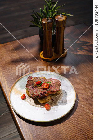 Steak with potatoes and cherry tomatoes on a wooden table in a restaurant 139792444