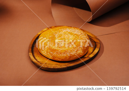Round bread sits on a wooden board during daylight in a simple setting 139792514