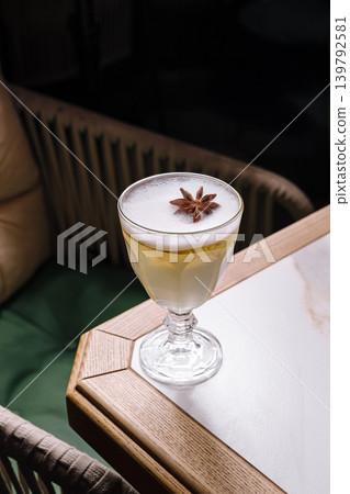 Elegant cocktail with foam and star anise garnish on a table in a cozy setting at night Elegant cocktail with foam and star anise garnish on a table in a cozy setting at night 139792581