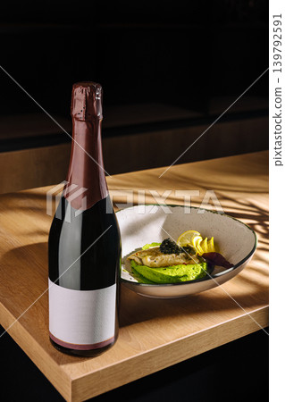 Bottle of sparkling wine next to a dish with avocado and caviar on a table Bottle of sparkling wine next to a dish with avocado and caviar on a table 139792591