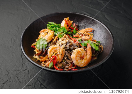 A bowl holds a mix of shrimp and noodles, topped with fresh herbs and spices A bowl holds a mix of shrimp and noodles, topped with fresh herbs and spices 139792674