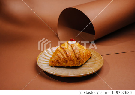 Croissant with cherry on top served on a plate with brown background Croissant with cherry on top served on a plate with brown background 139792686