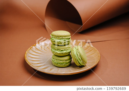 Green macarons stacked on a plate with brown background and paper roll Green macarons stacked on a plate with brown background and paper roll 139792689
