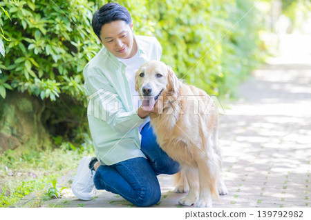 一名男子正在遛他的寵物狗,一隻體型較大的金毛犬。 一名男子正在遛他的寵物狗,一隻體型較大的金毛犬。 139792982