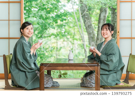 一位女士和她的朋友穿著浴衣,在一家傳統日式旅館的日式房間裡喝清酒。 一位女士和她的朋友穿著浴衣,在一家傳統日式旅館的日式房間裡喝清酒。 139793275