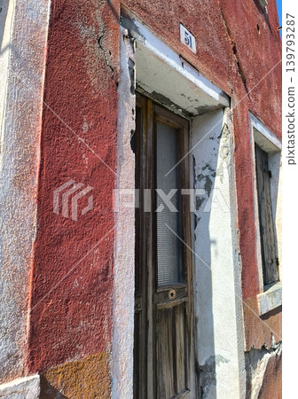A close-up of the old, colorful red entrance of a house on Burano Island. A close-up of the old, colorful red entrance of a house on Burano Island. 139793287