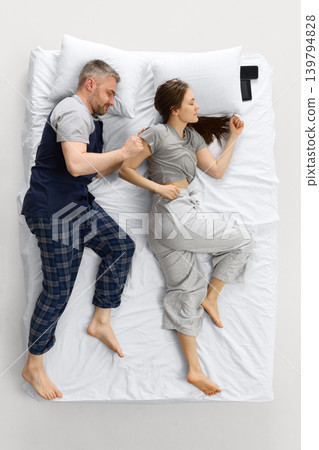Couple sleeping in running pose on white bed from overhead view with phones near pillows. Couple sleeping in running pose on white bed from overhead view with phones near pillows. 139794828