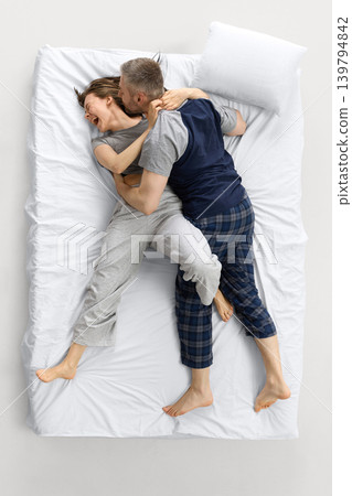 Laughing couple cuddling on white bed from overhead view 139794842