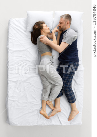 Overhead view playful couple lying on white bed and laughing together. Overhead view playful couple lying on white bed and laughing together. 139794846