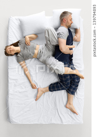 Couple sleeping in tangled pose on white bed from overhead view. Couple sleeping in tangled pose on white bed from overhead view. 139794893