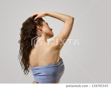 Woman showing wet curly hair texture from back in minimal beauty studio Woman showing wet curly hair texture from back in minimal beauty studio 139795545