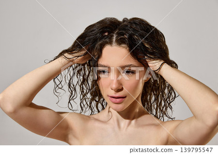 Woman massaging wet curly hair roots during moisturizing hair care routine. Woman massaging wet curly hair roots during moisturizing hair care routine. 139795547