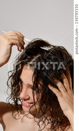Woman lifting wet curly hair roots with white hair brush during styling routine. Woman lifting wet curly hair roots with white hair brush during styling routine. 139795550