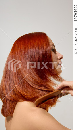 Woman combing smooth copper red hair after shine care treatment. Woman combing smooth copper red hair after shine care treatment. 139795692