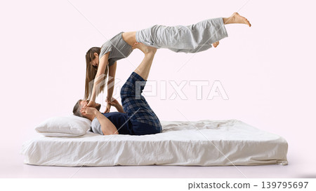 Man lifting woman above him on white bed from side view on pink background. Man lifting woman above him on white bed from side view on pink background. 139795697
